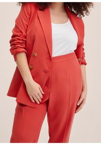 Red tailored blazer with double buttons and rolled sleeves, paired with matching high-waisted trousers. White fitted tank top underneath.
