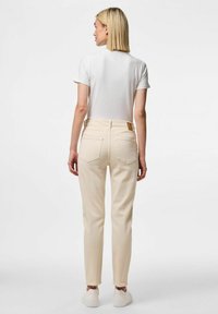 Beežid teksad otse lõikega, millel on kaks tagataskut ja nahkstripi silt vööl. Kombineeritud valge lühikese varrukaga T-särgiga.