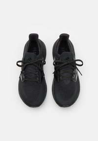Une paire de baskets de sport noires avec des tiges en tricot et des lacets, vues de dessus sur un fond blanc.