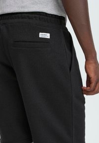 Pantalones cortos deportivos negros con una textura suave, que cuentan con una cinturilla elástica, bolsillos laterales y un bolsillo trasero con una etiqueta.
