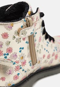 Bottines à imprimé floral en matériau brillant avec une base crème, ornées de fleurs roses et bleues, avec une fermeture éclair sur le côté et des lacets noirs.
