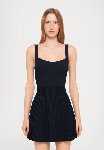 Robe en jersey marine avec de larges bretelles, corsage ajusté et jupette évasée dotée de plis verticaux pour plus de texture.