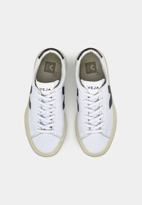 Biele plátené tenisky s čiernymi akcentmi, šnurovacie predné, okrúhla špička a gumová podrážka. Logo "VEJA" na jazyku a na strane. Minimalistický dizajn.