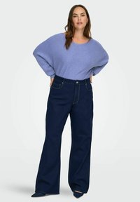 Hele sinine soonikkoes kampsun laiade varrukatega, millele on lisatud tumedasinised kõrge vöökohaga teksad kuldsete õmblustega ja lõdva lõikega.