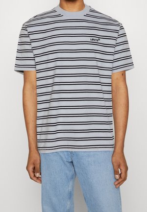 Mann trägt ein hellgraues T-Shirt mit horizontalen schwarzen Streifen und kleinem schwarzem Levi's-Logo auf der linken Brust, kombiniert mit hellblauen Jeans.