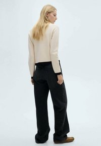 Light beige cropped sweater with black trim, paired with high-waisted black wide-leg jeans, viewed from the back against a light background.