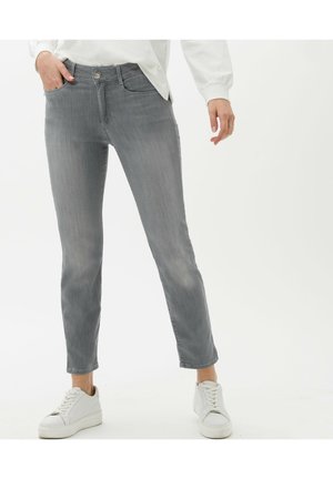 Jean slim gris en denim, avec une fermeture à bouton sur le devant, des poches latérales et un léger délavage. Associés à des baskets blanches.