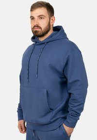 Felpa blu in cotone con tasca frontale, cappuccio con cordini, polsini a coste e una superficie liscia. Design minimalista con branding discreto.