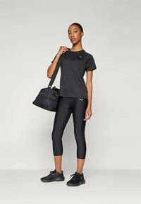 Must elastsest sportlikust riietusest koosnev must komplekt, mis sisaldab liibuvat T-särki ja retuusse. Materjal tundub veniv; komplektis on must spordikott ja mustad tennised.