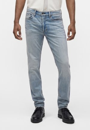 Mand iført lyseblå slim fit jeans kombineret med sorte snørebåndssko og en hvid skjorte stukket ned.