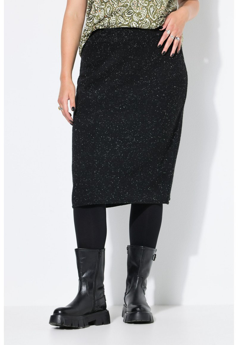 Schwarze knielange Rock mit einem strukturierten Strickmuster, ergänzt durch schwarze Strumpfhosen und schwarze Lederstiefel mit dickem Absatz.