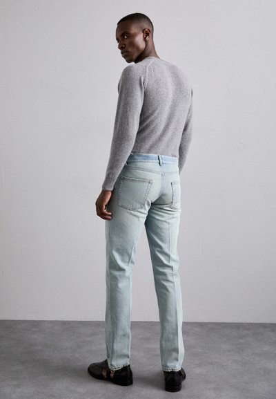 Maglione grigio, jeans azzurri chiari, scarpe nere. Il maglione presenta un colletto rotondo e polsini a coste; i jeans hanno una vestibilità dritta e tasche a toppa.