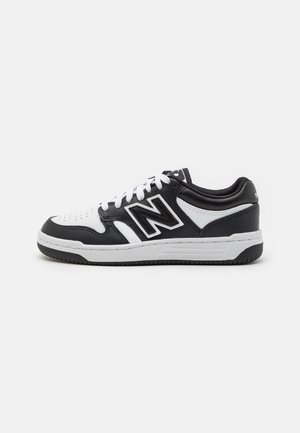 Scarpa da ginnastica New Balance bassa in bianco e nero con chiusura con lacci e suola in gomma, mostrata di lato su sfondo bianco.