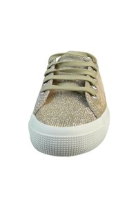Beżowe sneakersy z błyszczącego materiału, biała gumowa podeszwa i płaskie sznurowadła. Cechy to zaokrąglony czubek oraz teksturowany wzór na podeszwie.
