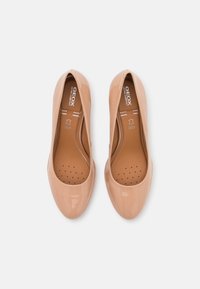 Escarpins en cuir verni nude avec bout arrondi, semelle intérieure perforée et amorti interne. Logo de la marque visible sur la semelle intérieure.