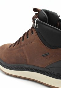 Bota alta de piel marrón con cuello de tela negra, suela de goma, ojales de metal y detalle de entresuela texturizado. Cordones en marrón a juego.