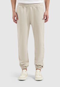 Lichtbeige joggingsbroek met een elastische tailleband en boorden, voorzien van een subtiele logodetail op de linker bovenbeen, gemaakt van zachte, gestructureerde stof.