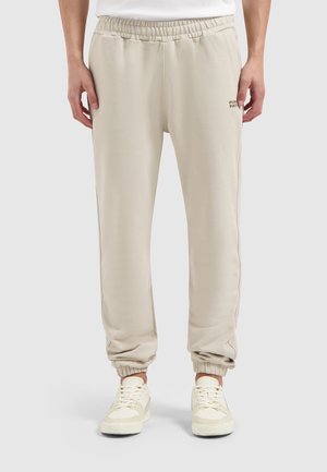 Helle beigefarbene Sweatpants mit elastischem Bund und Bündchen, versehen mit einem dezenten Logo-Detail am linken Oberschenkel, aus weichem, strukturiertem Stoff.