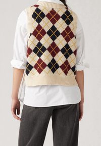 Gilet en maille crème avec un motif losangé multicolore comprenant des losanges bordeaux, marine et jaunes ; ourlet côtelé et design sans manches.