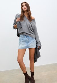 Överdimensionerad grå tröja, ljusblå denim minikjol, bruna ankelsockor och mörka skor. Modellen poserar mot en enfärgad bakgrund.