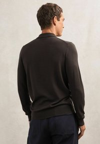 Brauner gestrickter Pullover mit langen Ärmeln, gerippten Bündchen und Saum, mit einer dezenten Textur. Dazu getragen mit dunkelblauen Hosen.