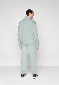 Világoszöld pulóver és hozzáillő nadrág, puha anyagból, magas nyakkal és bordázott mandzsettákkal. A megjelenést fekete sportcipő teszi teljessé.