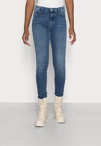 Vaqueros ajustados de color azul con cintura alta, que incluyen bolsillos delanteros y cremallera, combinados con botas de combate color crema con cordones.