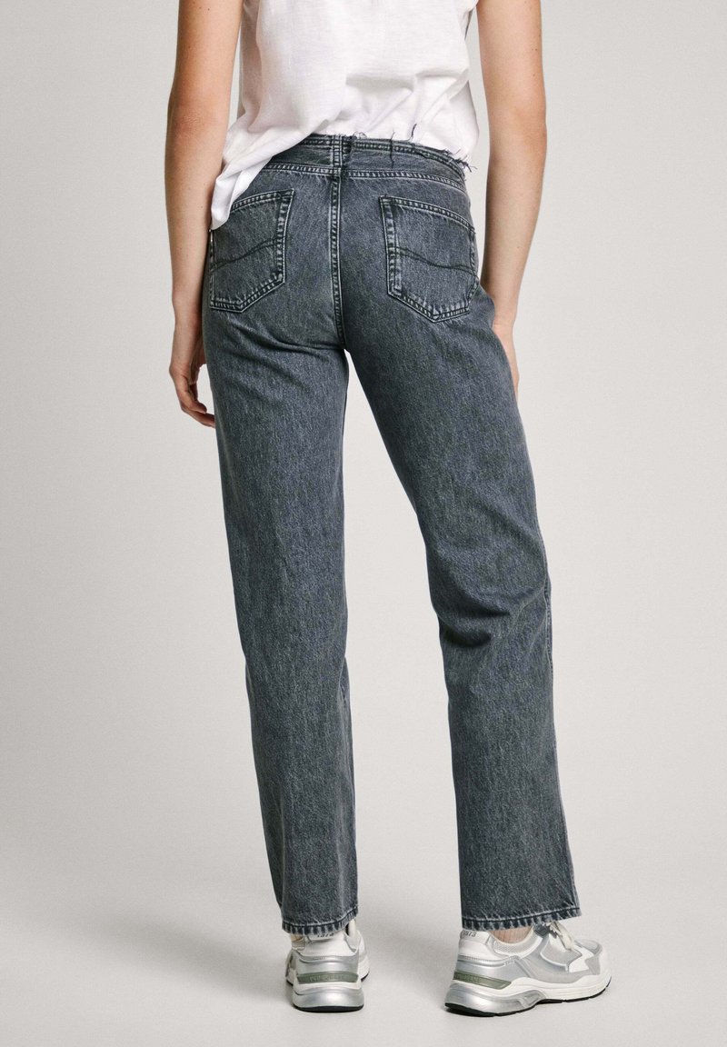 Dunkelgraue Jeans aus Denim mit geradem Bein und ausgefranstem Saum, ausgestattet mit zwei Gesäßtaschen und einem hoch geschnittenen Design. Getragen mit silbernen Sneakers.