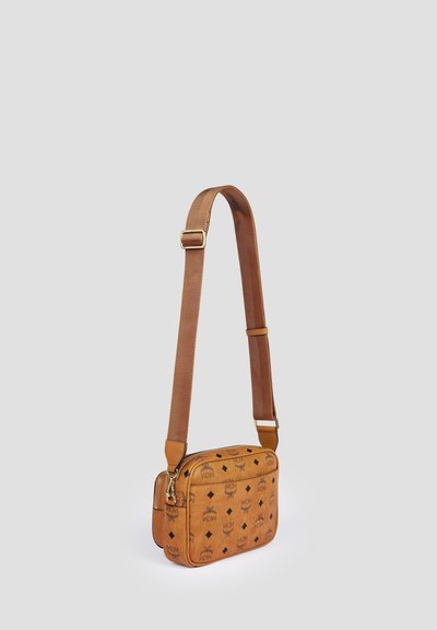 Light brown leather crossbody bag with adjustable strap and black logo pattern on smooth surface, standing upright on plain background.