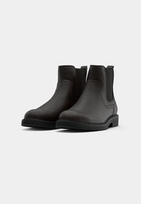 Brown leather Chelsea boots with elastic side panels, rounded toes, and a textured rubber sole. Smooth finish and minimal stitching details.