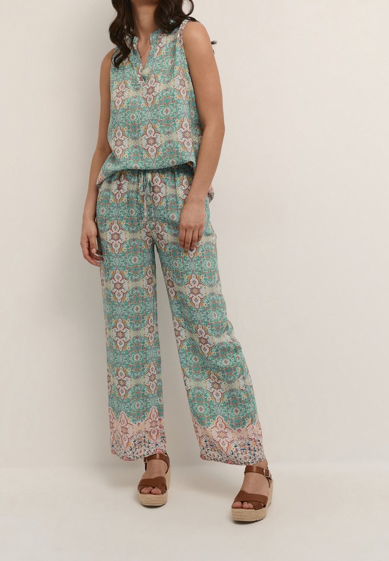 Floral patterned sleeveless top with a v-neck, paired with wide-leg trousers. Colorful turquoise with peach accents and light fabric texture.