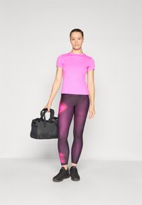 Rozā īsām piedurknēm pieguloša blūze, melni sporta legingi ar purpura gradienta rakstu, un melna sporta soma ar divām rokturiem. Melni sporta apavi.