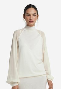 Top bianco a collo alto con maniche lunghe trasparenti, caratterizzato da una vestibilità rilassata e una consistenza morbida, che mette in risalto un design minimalista con dettagli sottili.