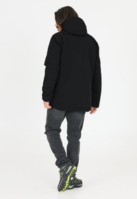 Sort hættetrøje med mat finish, lange ærmer og afslappet pasform, parret med mørkegrå jeans og sort-grønne træningssko.