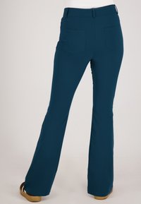 Teal flarebroek van gladde stof, met twee achterzakken en een platte tailleband, getoond van achter.