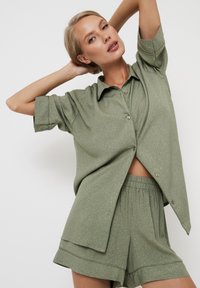 Conjunto de loungewear en verde oliva que incluye una camisa de botones de manga corta y pantalones cortos con cintura elástica, fabricado en una tela texturizada con patrones sutiles.