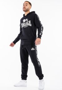 Black hoodie and joggers set from Lonsdale, featuring a logo print, contrasting white accents, and a soft fabric finish. Standard fit design.