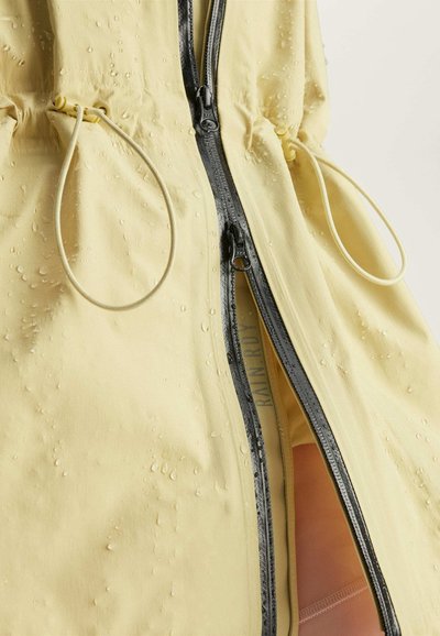 Chaqueta impermeable amarilla con cremallera frontal, detalles de cordón y gotas de agua en la superficie, que muestra una textura suave.
