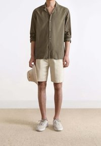 Olive green button-up shirt with a textured pattern, paired with light beige shorts, and gray-and-white sneakers. White background.