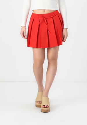 Red pleated skirt with a drawstring waist. Worn with beige platform shoes featuring a wooden sole and open toe design.