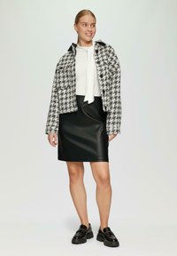 Zwart-wit houndstooth jasje met een kraagontwerp, gecombineerd met een zwarte faux leren rok en chunky zwarte loafers.