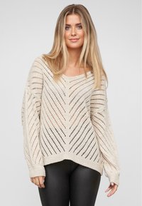 Beige gestrickter Pullover mit lockerer Passform, Zickzackmuster, weiten Ärmeln und geripptem Saum. Die strukturierte, halbtransparente Webart sorgt für visuelles Interesse.