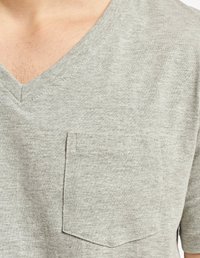 Pilkos spalvos trumpas rankovėmis V formos iškirptės marškinėliai, pagaminti iš minkštos medžiagos, turintys kišenę kairėje pusėje ir tekstūruotą išvaizdą.