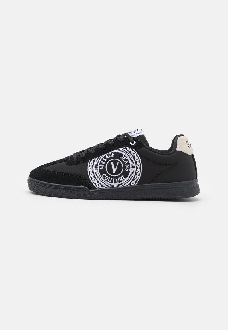 Schwarzer Sneaker mit niedrigem Schaft und schwarzen Schnürsenkeln, weißem rundem "Versace Jeans Couture"-Logo an der Seite und hellbeigem Fersenlasche.