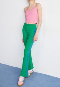 Gröna utsvängda byxor med blå sidostripes, kombinerat med en rosa ribbad crop top och rosa sneakers med gröna detaljer. Slät tygtextur.