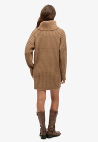 Vestito a maglia marrone a coste con collo alto, maniche lunghe e vestibilità comoda, abbinato a stivali alti in pelle marrone.