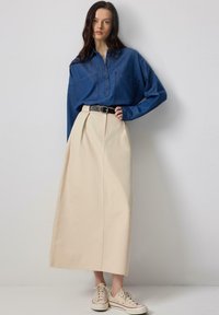 Blue denim shirt with button-down front, paired with a beige high-waisted skirt and white sneakers. Simple design with a relaxed fit.