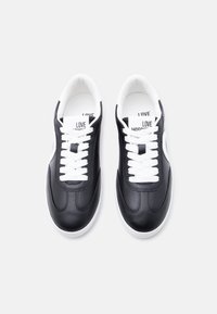 Ζευγάρι μαύρα χαμηλά αθλητικά παπούτσια με λευκά κορδόνια, λευκές σόλες και λογότυπο "LOVE MOSCHINO" στη γλώσσα και την εσωτερική σόλα.