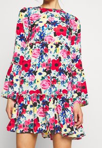 Robe florale à manches longues, arborant un mélange de fleurs roses, rouges et bleues sur un fond jaune. Ourlet volanté et détail de taille élastique.