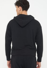 Black hooded sweatshirt with long sleeves, ribbed cuffs, and a ribbed hem. Fabric is a soft, textured material. No visible logos or patterns.
